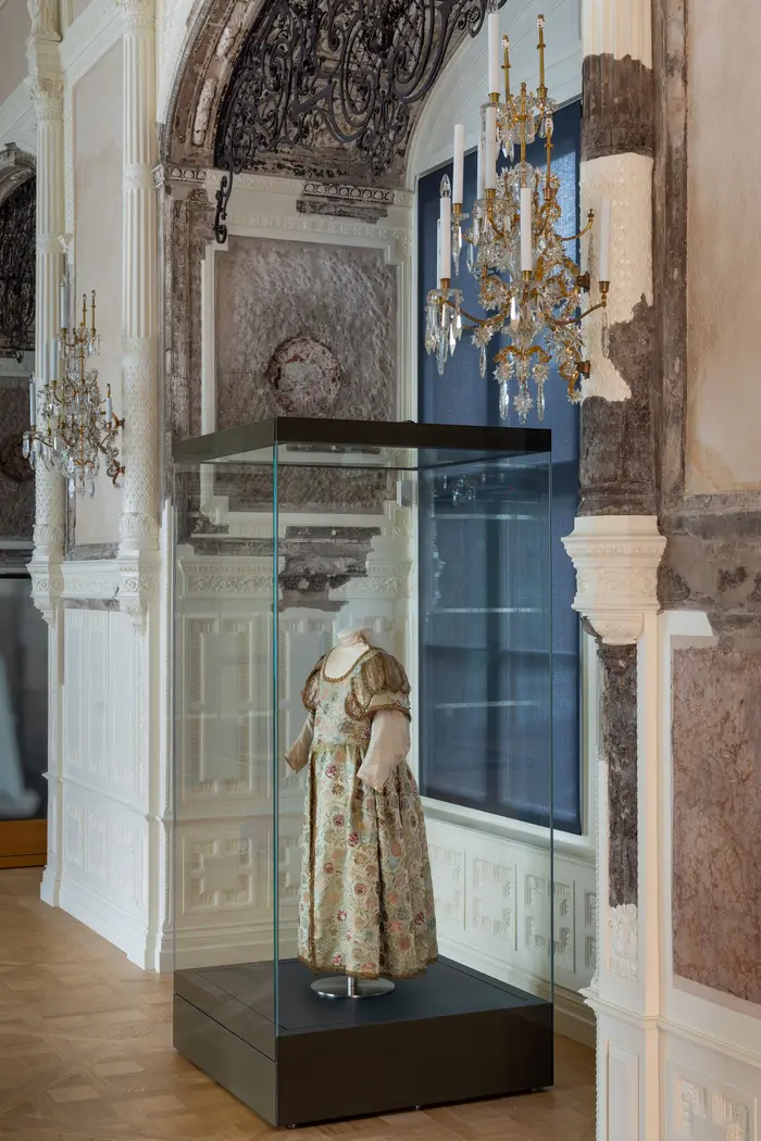 Raumansicht mit einem prunkvollen Kinderkleid in einer Vitrine
