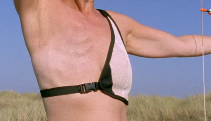 Es ist der Oberkörper einer weiblich gelesenen Person zu sehen, mit amputierter Brust, die im Begriff ist den Bogen zu spannen und einen Pfeil zu schießen.