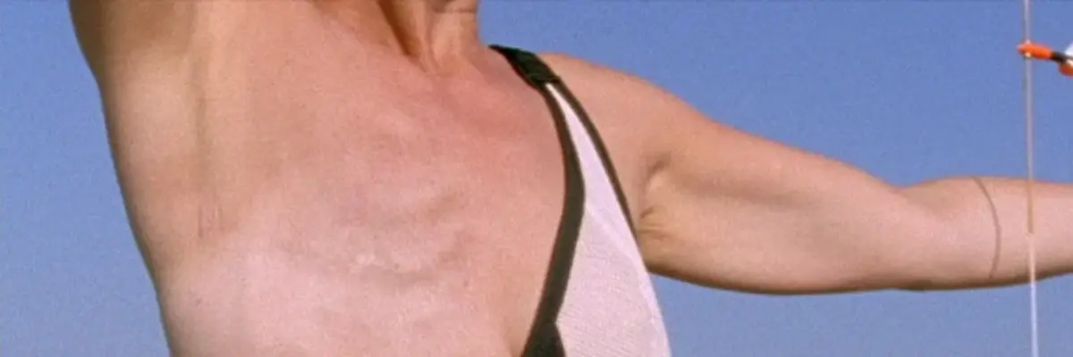 Es ist der Oberkörper einer weiblich gelesenen Person zu sehen, mit amputierter Brust, die im Begriff ist den Bogen zu spannen und einen Pfeil zu schießen.